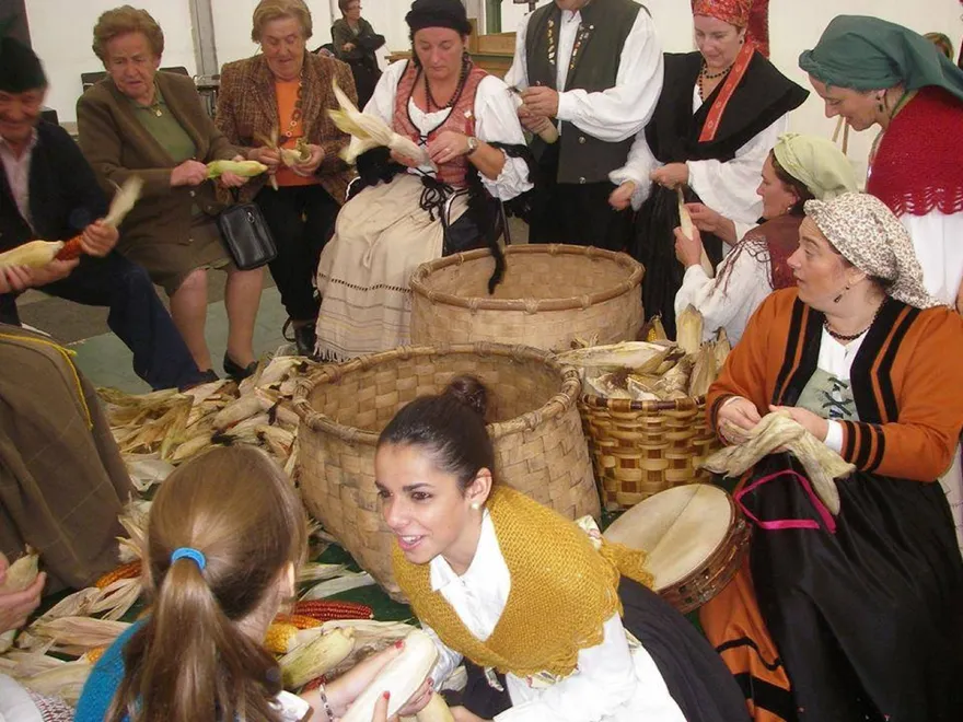 Vecinas y vecinos con traje tradicional asturiano deshojando maíz en la esfoyaza
